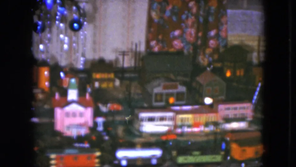 1951 Cleveland home-movie frame of a model train scene with a church-like building, miniature shops, and Christmas ornaments above the layout.