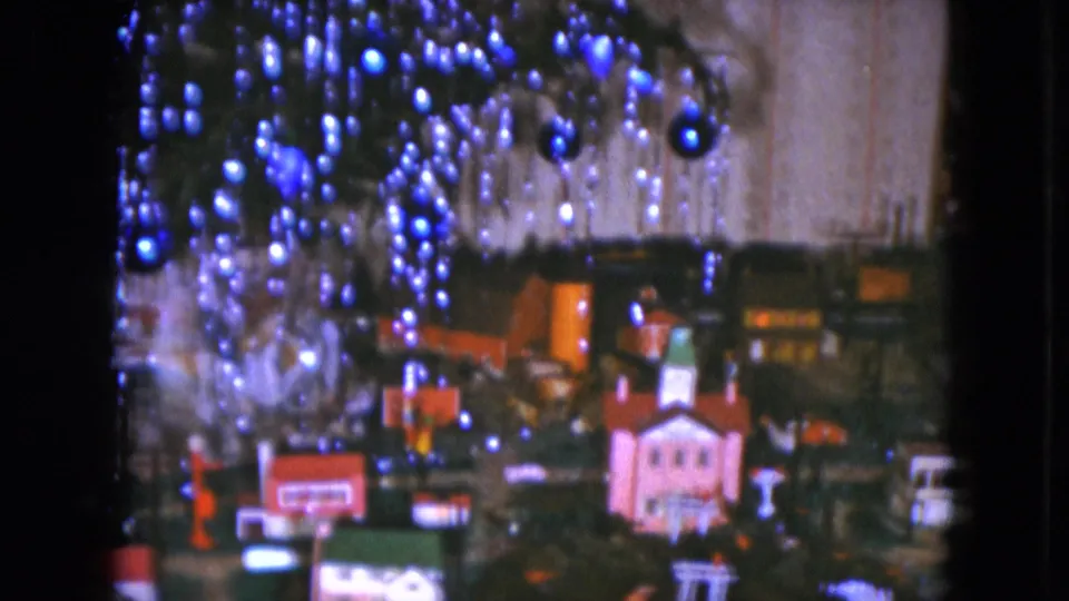 1951 Cleveland home-movie frame with blue ornaments over a miniature town and model train layout, seen in soft 8mm color.