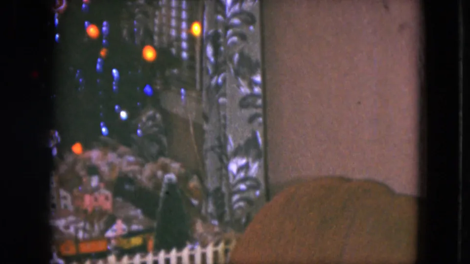 1951 Cleveland home-movie frame showing miniature train scenery under a Christmas tree with colored lights and patterned curtains.