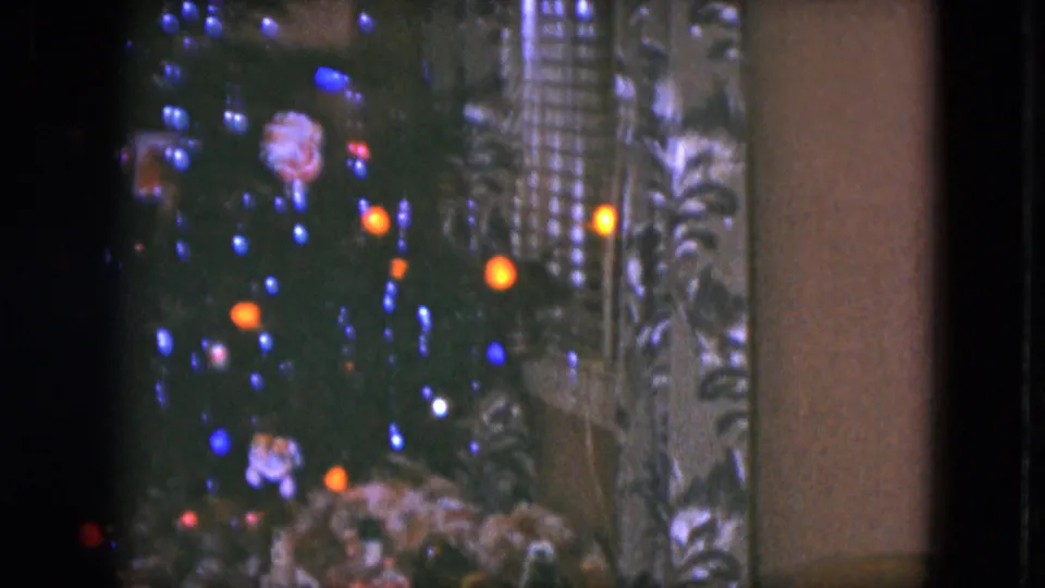 1951 Cleveland home-movie frame showing a closer view of the lit Christmas tree, patterned curtain, and toy-train scenery at the bottom edge.