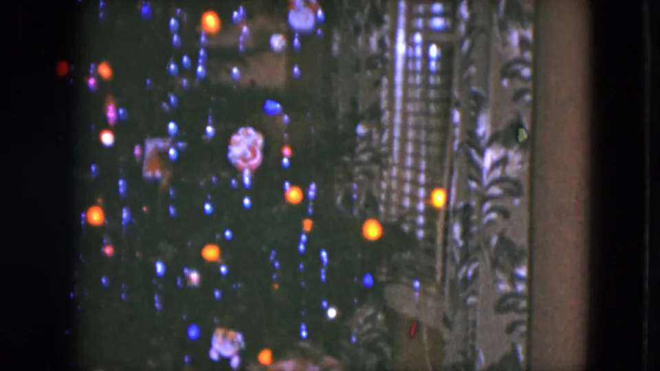 1951 Cleveland home-movie frame showing colored Christmas tree lights, patterned curtains, and small train-set scenery near the lower edge.