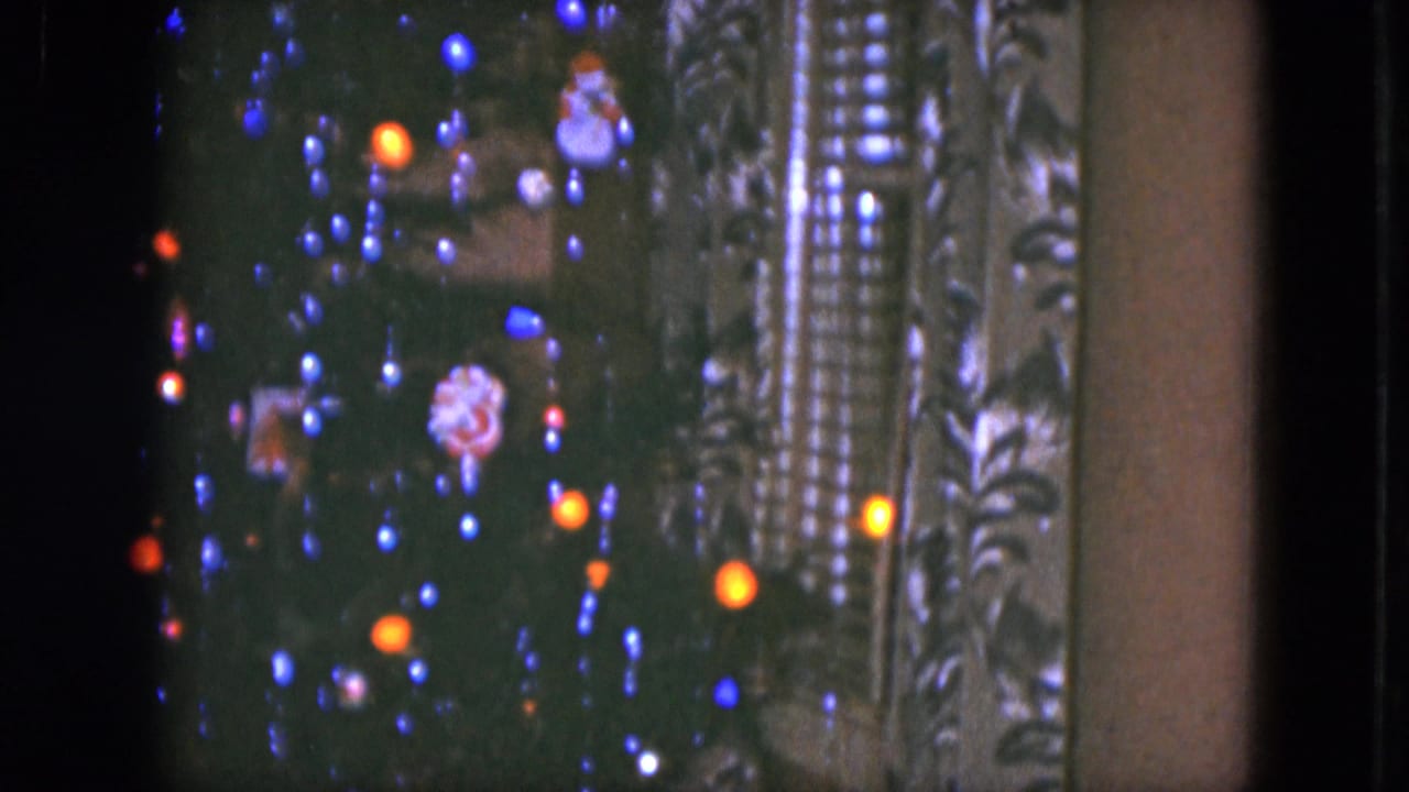 Close view of a Christmas tree with colored lights, ornaments, and a Santa decoration beside patterned curtains.