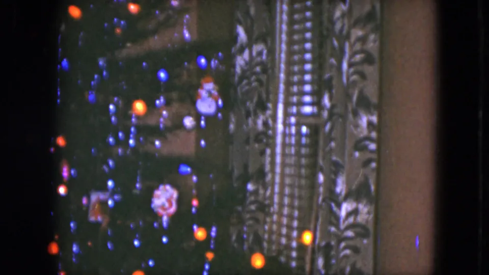 1951 Cleveland 8mm frame of a Christmas tree with colored lights and ornaments, framed tightly against patterned indoor curtains.
