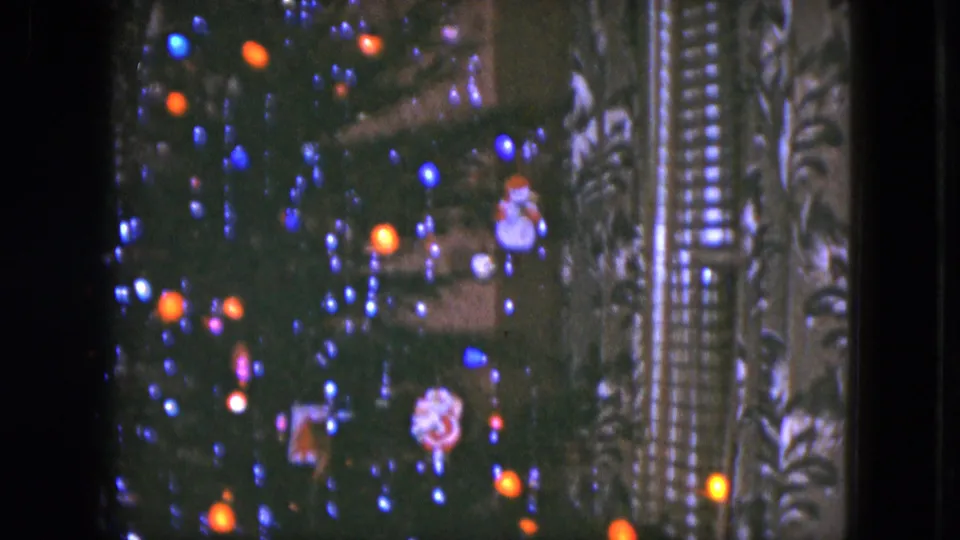 Soft 8mm frame from the 1951 Cleveland clip showing Christmas tree branches, colored lights, ornaments, and nearby patterned drapery.