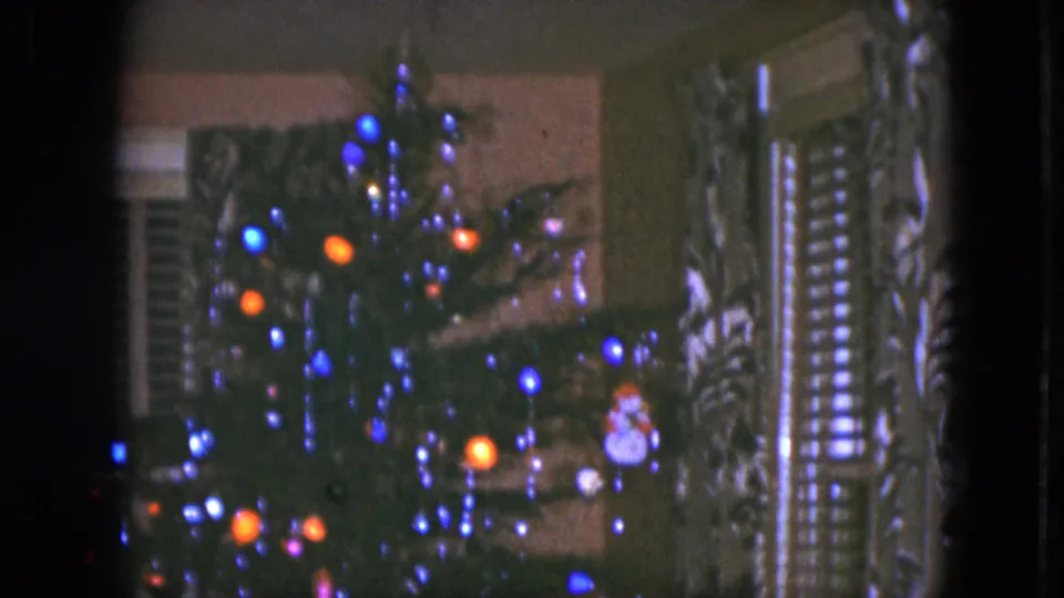 1951 Cleveland home-movie frame showing a decorated Christmas tree with glowing blue and orange lights near window shutters.