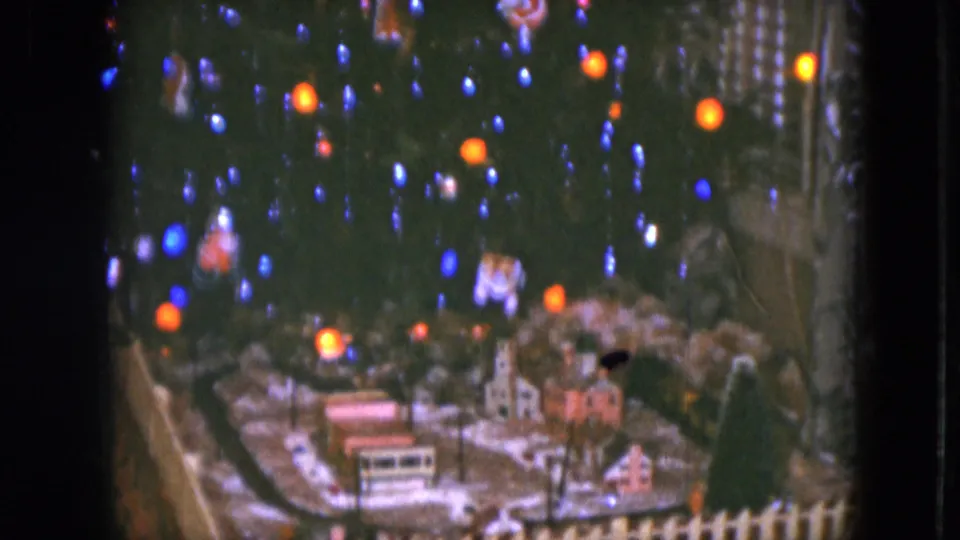 1951 Cleveland home-movie frame with a train-set village, small houses, track area, and colored tree lights above.