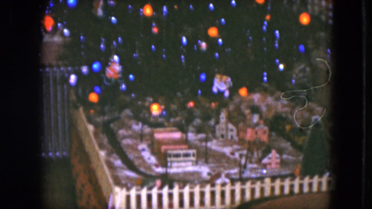 Miniature Christmas village and train layout beneath colored tree lights.
