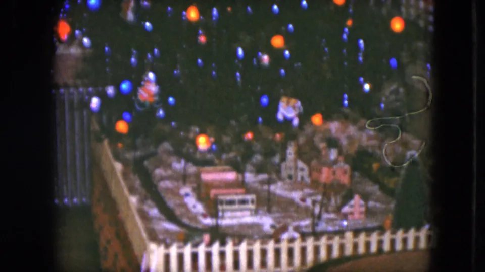 1951 Cleveland home-movie frame showing a small Christmas train village under glowing blue and orange tree lights.