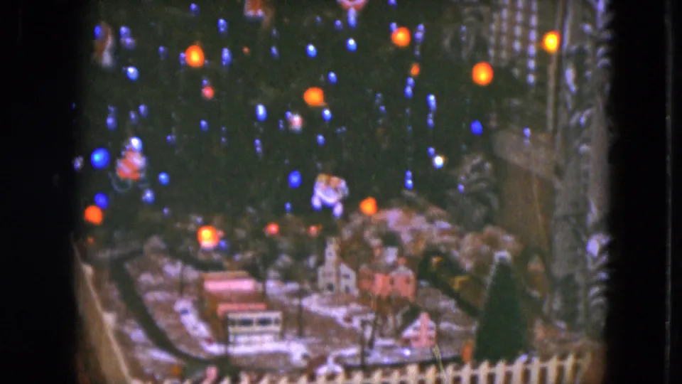 A Cleveland 1951 holiday display shows model buildings, fence, and train track beneath a low-lit Christmas tree.