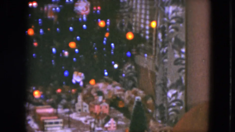 1951 Cleveland home-movie still with colored tree lights above a small Christmas village and model train scene.