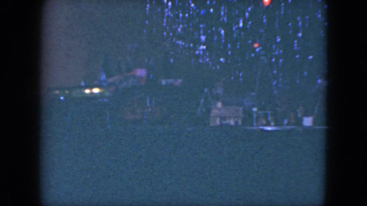 1951 Cleveland home-movie frame showing a lit Christmas tree and small model railroad scene in a dark room.