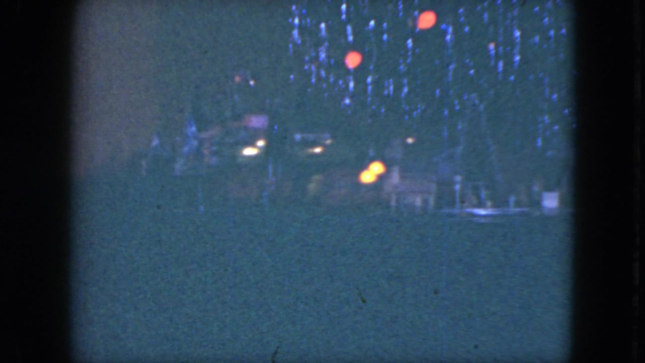 Blue-tinted 8mm frame from Cleveland, 1951, with a small train passing below tree lights and red ornaments.