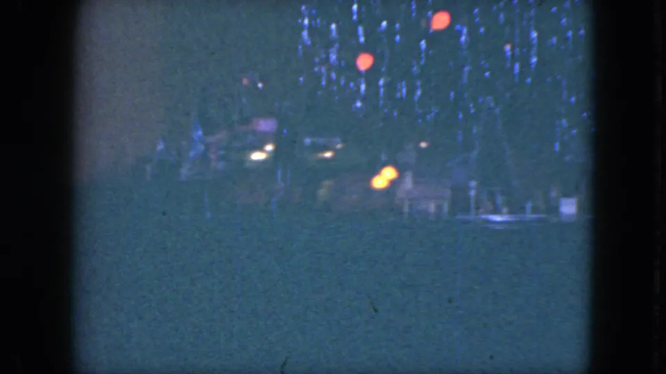 Blue-tinted 8mm frame from Cleveland, 1951, with a small train passing below tree lights and red ornaments.