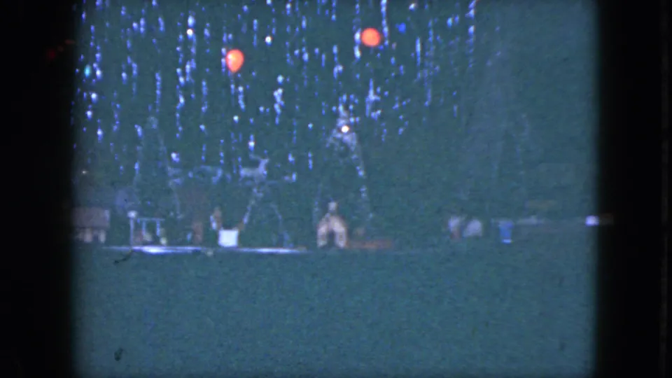 1951 Cleveland 8mm frame of a Christmas tree base with lights, red ornaments, small decorations, and train-set scenery.