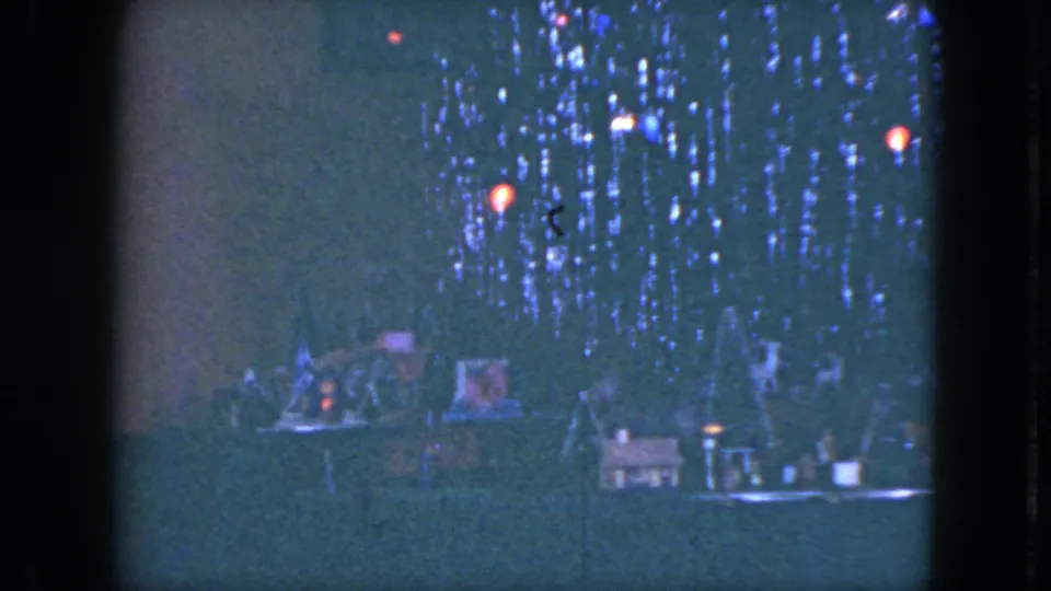 A low-light 1951 Cleveland frame shows the miniature train village, glowing holiday lights, and the woman partially obscured at the left edge.