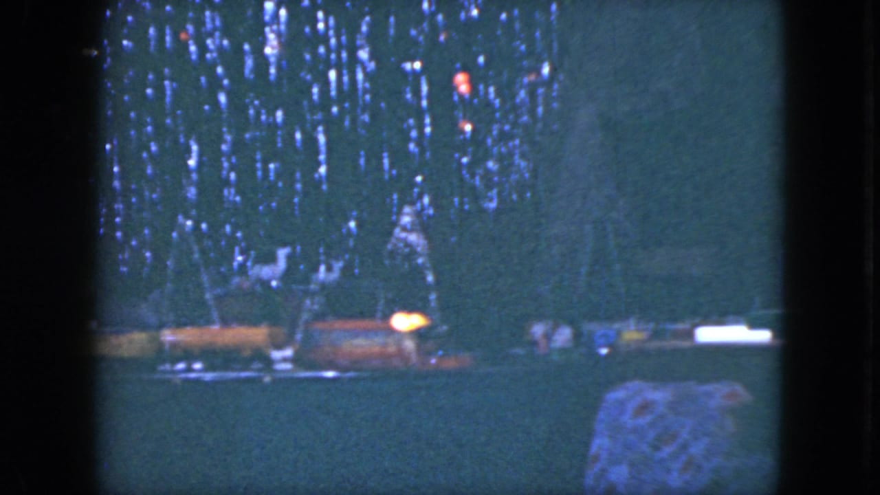 Model train layout beneath a dark decorated Christmas tree with colored lights.