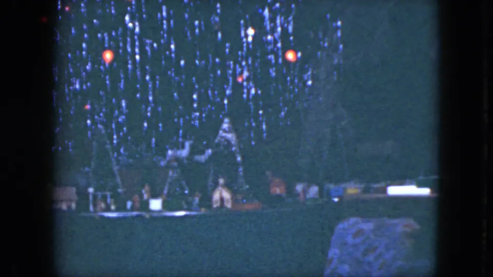 1951 Cleveland home-movie frame showing toy train scenery and small house forms beneath a decorated Christmas tree.