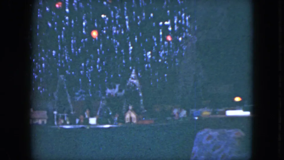1951 Cleveland frame of a model train display beneath a decorated Christmas tree, rendered in soft 8mm low light.
