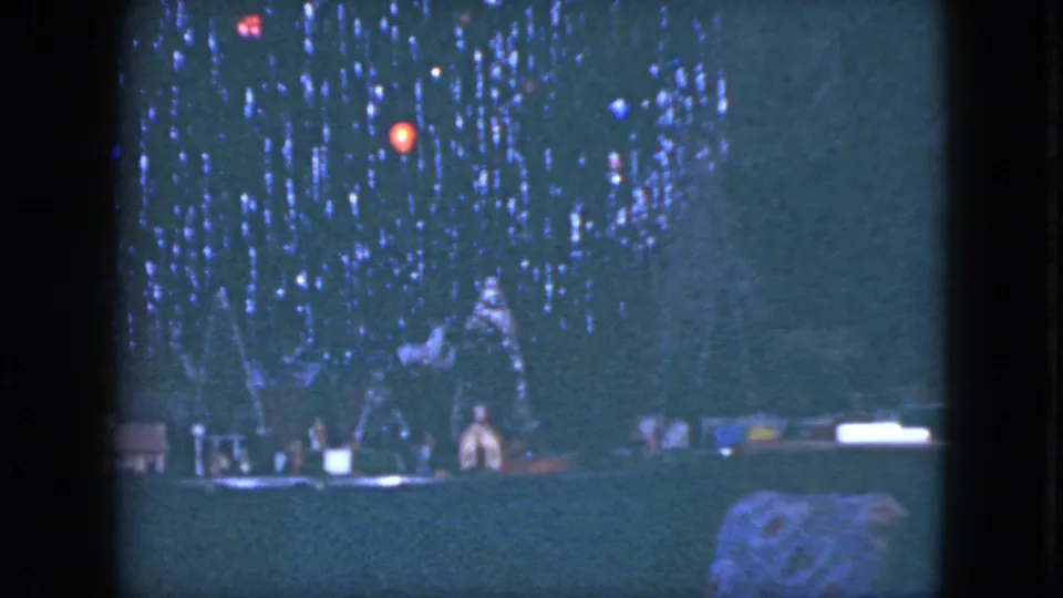 1951 Cleveland 8mm frame showing a dark Christmas tree with red and blue lights over small lit holiday structures.