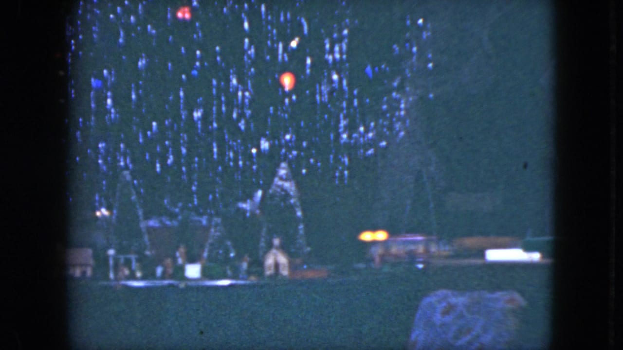 1951 Cleveland home-movie frame with a dim Christmas tree, glowing colored bulbs, and small structures along the base.
