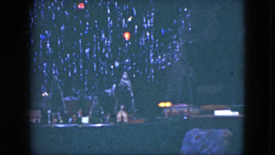1951 Cleveland home-movie frame with a dim Christmas tree, glowing colored bulbs, and small structures along the base.