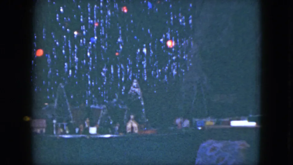1951 Cleveland home-movie frame of a dark Christmas tree with glowing colored bulbs and small lit display pieces below.