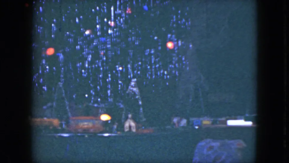 1951 Cleveland home-movie frame showing a small model train scene under a lit Christmas tree in low light.