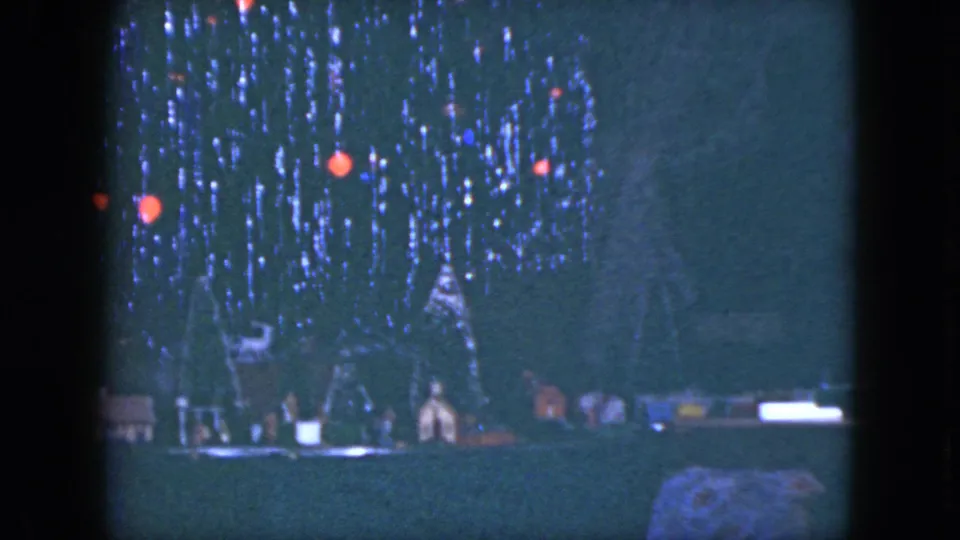 Low-light 1951 Cleveland holiday frame showing a model train arrangement beneath a decorated tree.