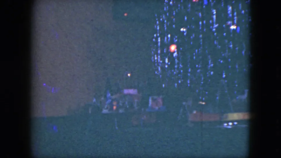 1951 Cleveland home-movie frame with a dim model train scene and colored lights under the tree.