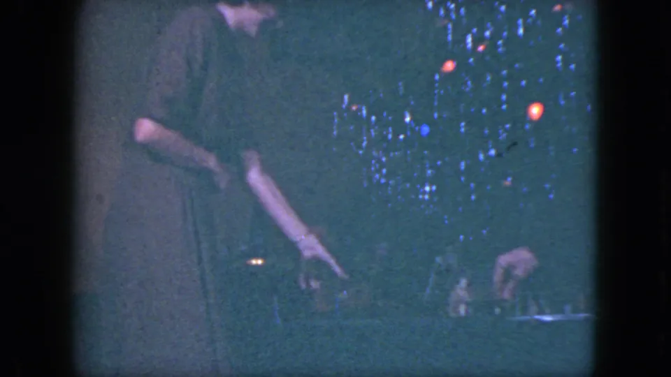 In this 1951 Cleveland home-movie frame, a woman in a dark dress reaches down beside the Christmas tree and train display.