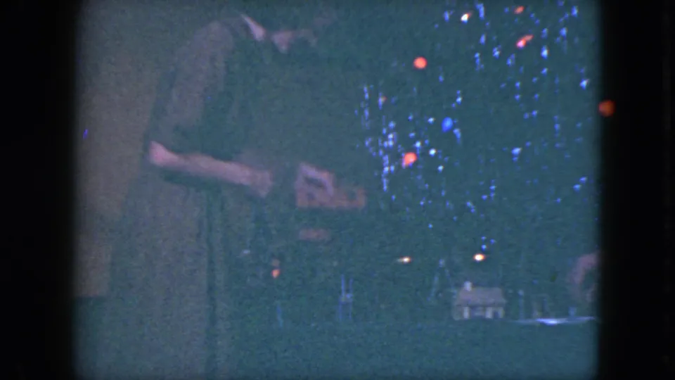 A woman appears beside the Christmas tree and model train display in a dim Cleveland holiday interior from 1951.