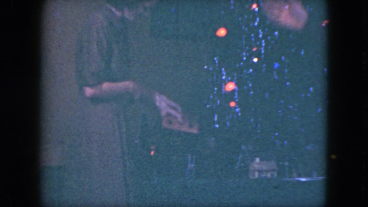 Woman's hands near a toy train layout with small scenery and glowing colored lights.