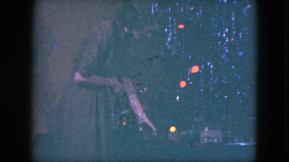 A partial frame shows the woman leaning near the miniature train display, with the home-movie exposure emphasizing the holiday lights.