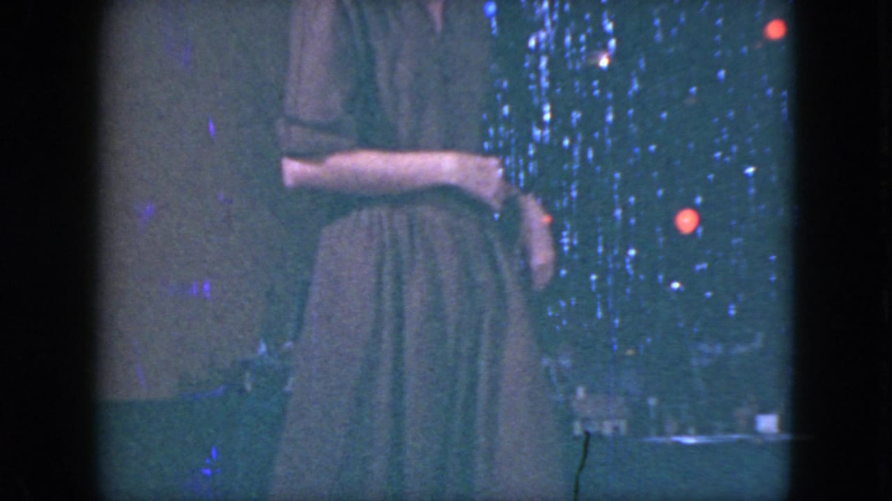 The woman stands near the miniature train setup in a Cleveland holiday interior, with tinsel and red-blue lights visible behind her.