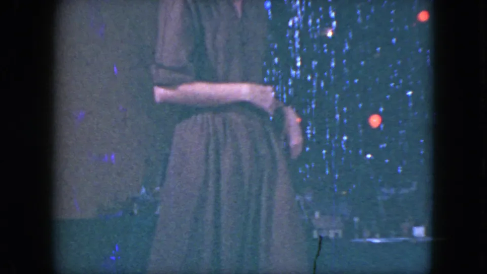 The woman stands near the miniature train setup in a Cleveland holiday interior, with tinsel and red-blue lights visible behind her.