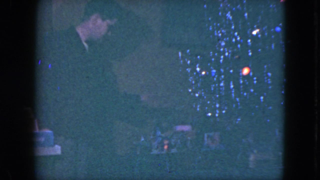 A dark-suited man appears to inspect the Christmas train setup near tree lights in the Cleveland 1951 home-movie footage.