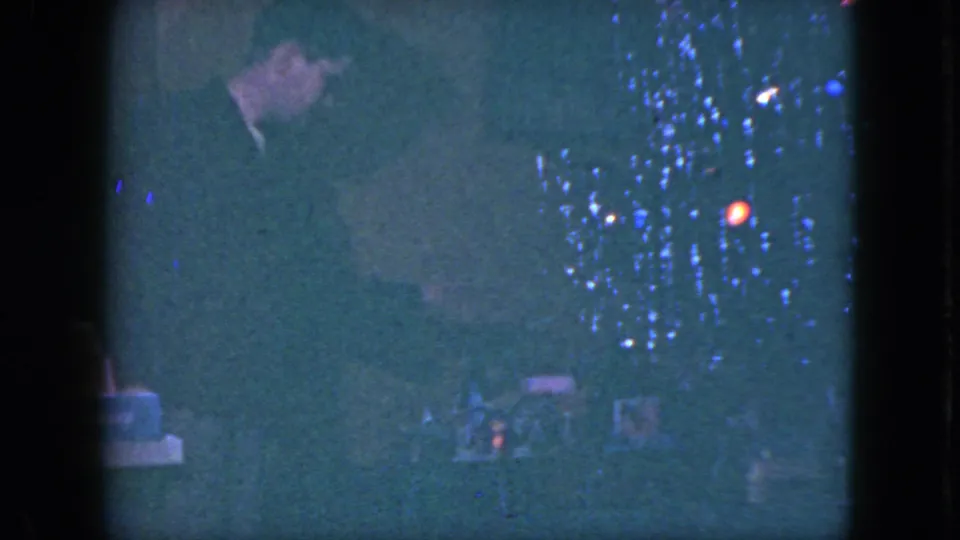 A dark-suited man appears to inspect the Christmas train setup near tree lights in the Cleveland 1951 home-movie footage.
