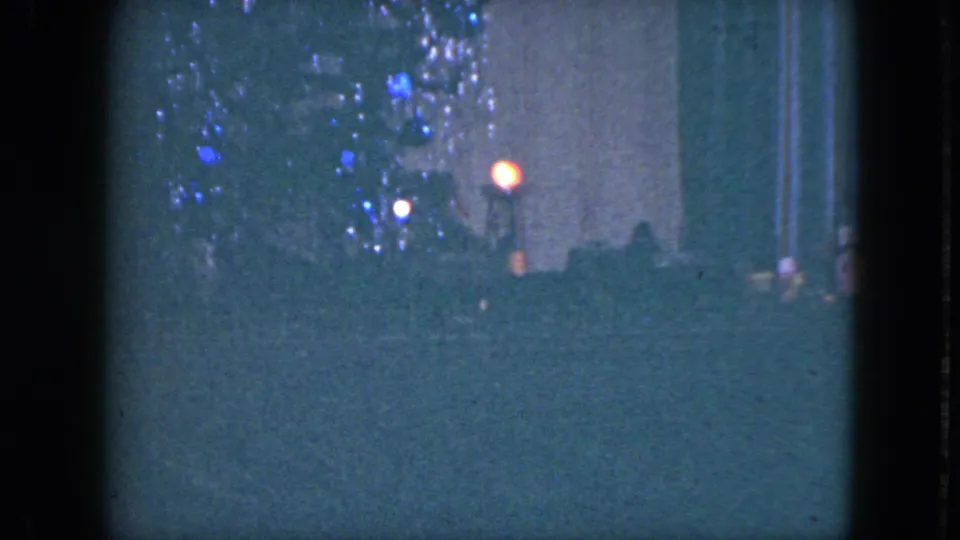 Low-light 1951 Cleveland home-movie frame showing blue holiday lights near a dark street with distant red and white lights.