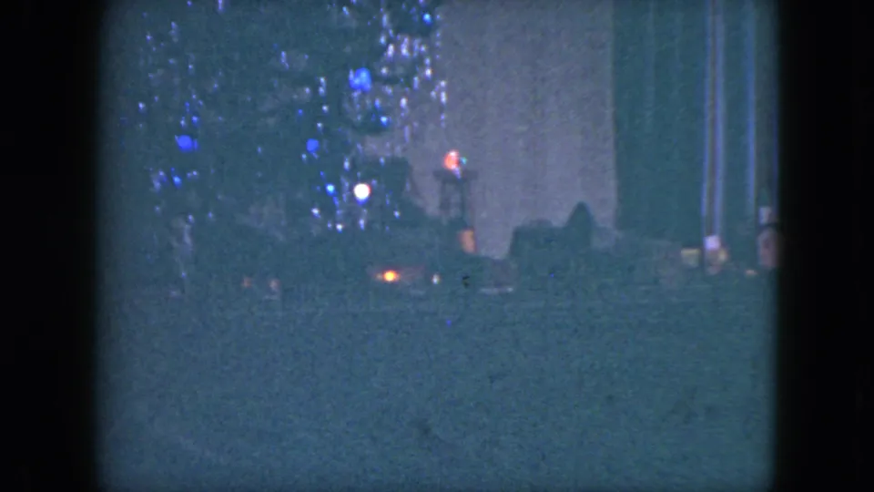 Grainy 1951 Cleveland frame with blue holiday lights and blurred red-orange points suggesting passing traffic at night.