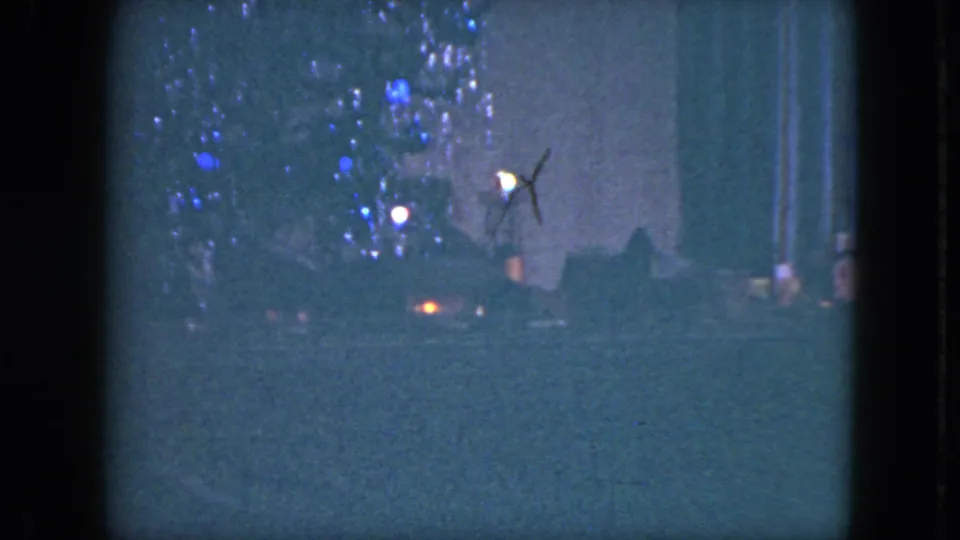 Low-light 1951 Cleveland home-movie frame showing blue holiday lights, a bright white point, and a small orange light near the street.