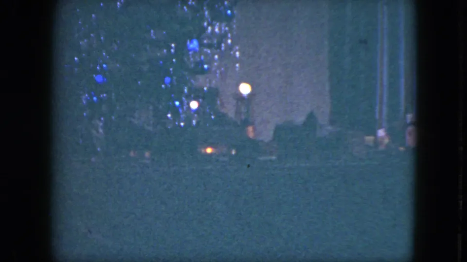1951 Cleveland home-movie frame showing a dim Christmas tree with silver tinsel, blue ornaments, and a toy train near the base.