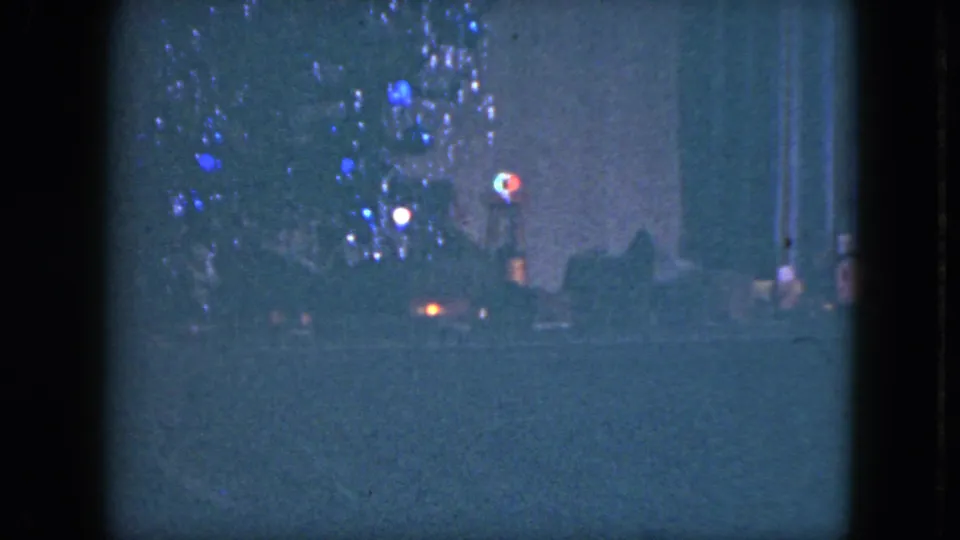 1951 home-movie still showing the toy train low in frame beneath a tinsel-covered Christmas tree in a Cleveland interior.