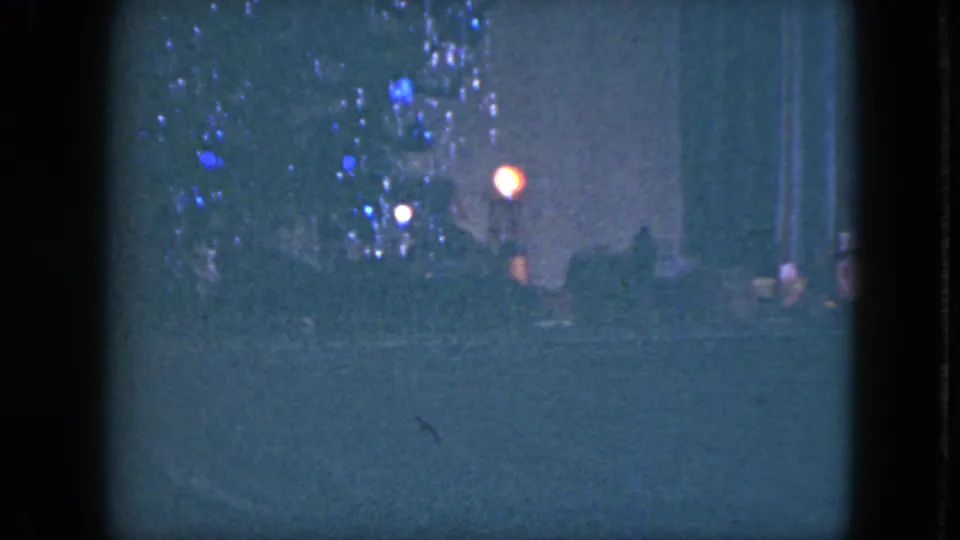 Blue-tinted 8mm frame of the Cleveland Christmas setup, with tinsel, ornaments, a bright tree light, and the toy train below.