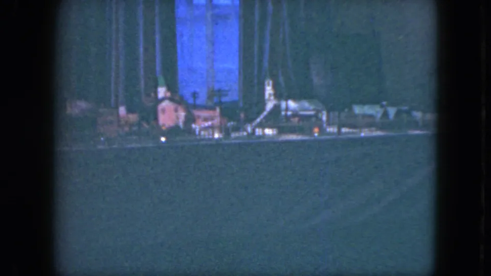 Cleveland 1951 home-movie frame of a small model village scene, with tree forms, tiny lit points, and the lower track area visible.