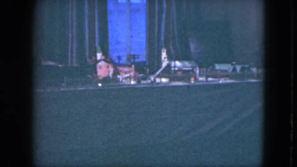 1951 Cleveland home-movie frame showing a dimly lit toy train layout with miniature buildings and visible rail lines.