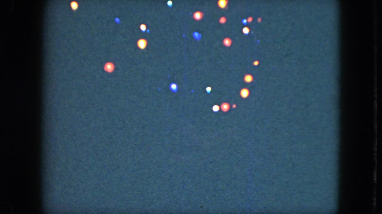 1951 Cleveland 8mm frame showing small colored lights scattered in a dark night sky with soft film grain.