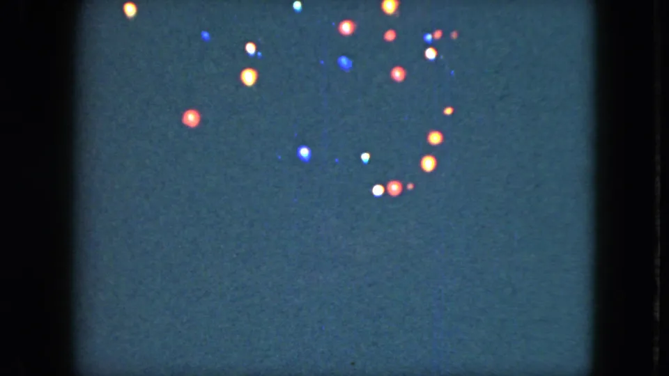 1951 Cleveland 8mm frame showing small colored lights scattered in a dark night sky with soft film grain.