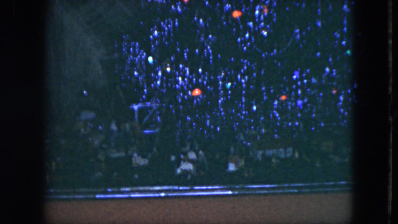 Tinsel-covered Christmas tree seen through a dark frame with small colored lights.