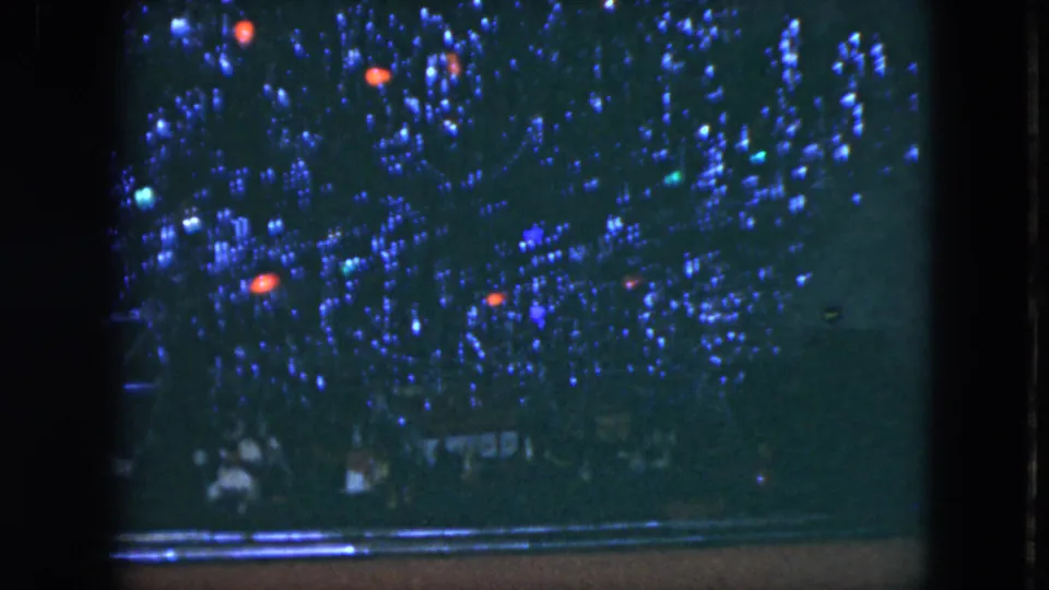 1951 Cleveland home-movie still of a Christmas tree filled with blue tinsel, red ornaments, and dim holiday lights.