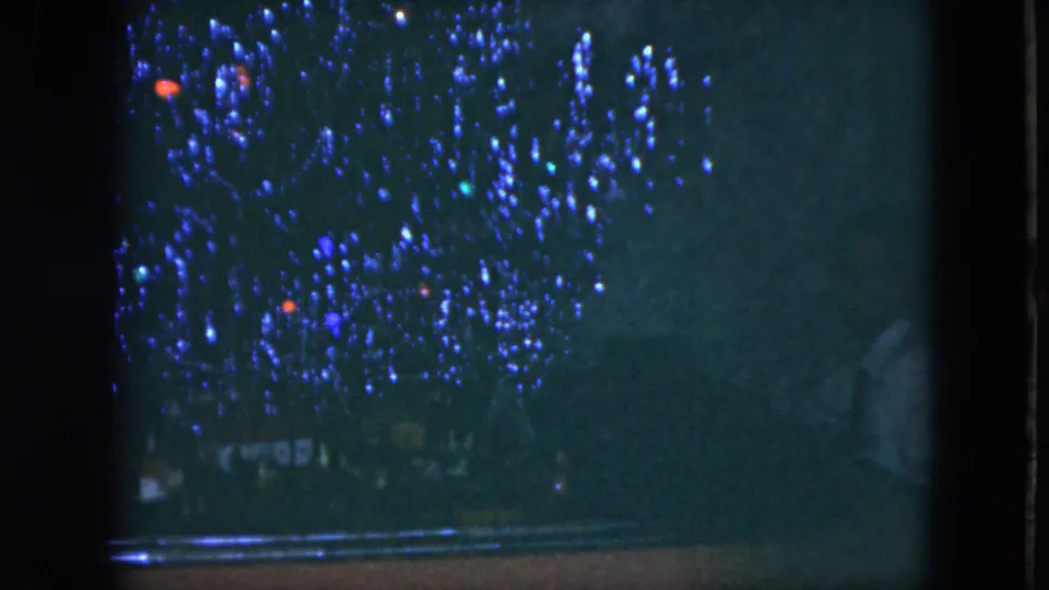 1951 Cleveland 8mm frame of a tinsel-covered Christmas tree, partly blocked by a dark vertical frame and soft shadow.